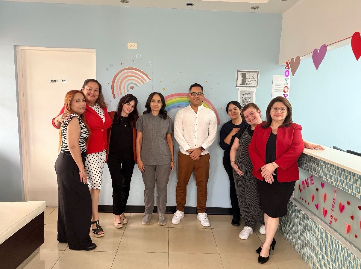 A group of colleagues standing together in a bright office with wall decorations.